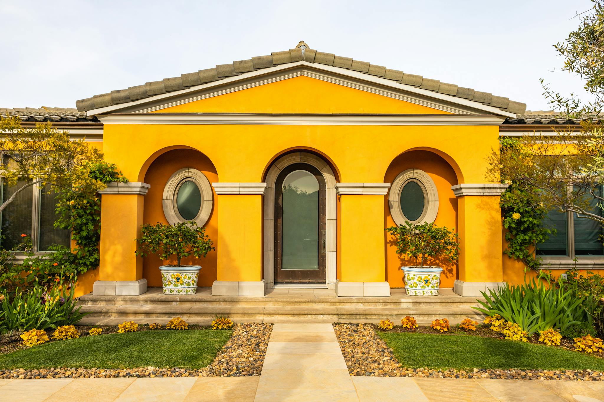Charming yellow villa entrance with lush garden and unique architectural details.